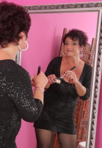 Vrela prezgodna matorka kratke crne kose pozira u seksi odeći pred ogledalom dok se šminka